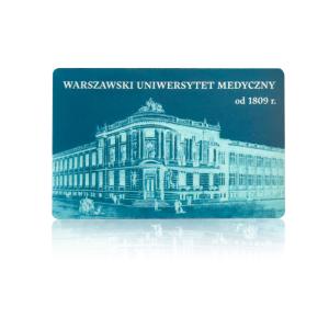 Prostokątny magnes w turkusowych kolorach. Centrum magnesu zajmuje zdjęcie Collegium Anatomicum WUM z XIX w. Jest to dwupiętrowy budynek z ozdobną fasadą, wieloma oknami oraz rzeźbami na fasadzie.