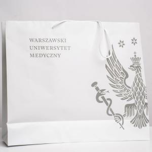 Biała prostokątna torba papierowa z białymi rączkami. Na torbie szary/srebrny logotyp WUM.
