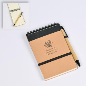 Prostokątny notes na czarnej spirali. Okładka notesu jest beżowa. Do notesu przyczepiony jest długopis w czarno-beżowych kolorach. Notes jest spięty czarną gumką. Na okładce jest czarny logotyp WUM.