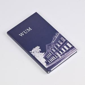 Prostokątny notes z granatową okładką, na której widnieje biały szkic starego dwupiętrowego budynku oraz drzewa i chodnika.